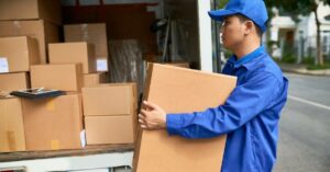 Delivery man carrying a box behind a delivery truck